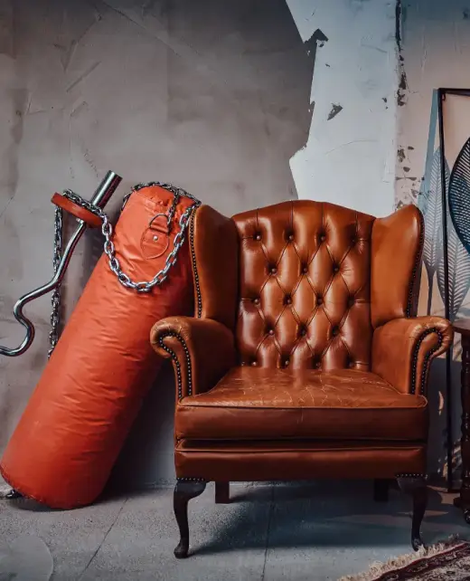 seat1 A vintage-style brown leather armchair with tufted leather upholstery, placed in a rustic industrial setting. Ideal for showcasing timeless furniture upholstery and elegant design for homes or offices in Bahrain.